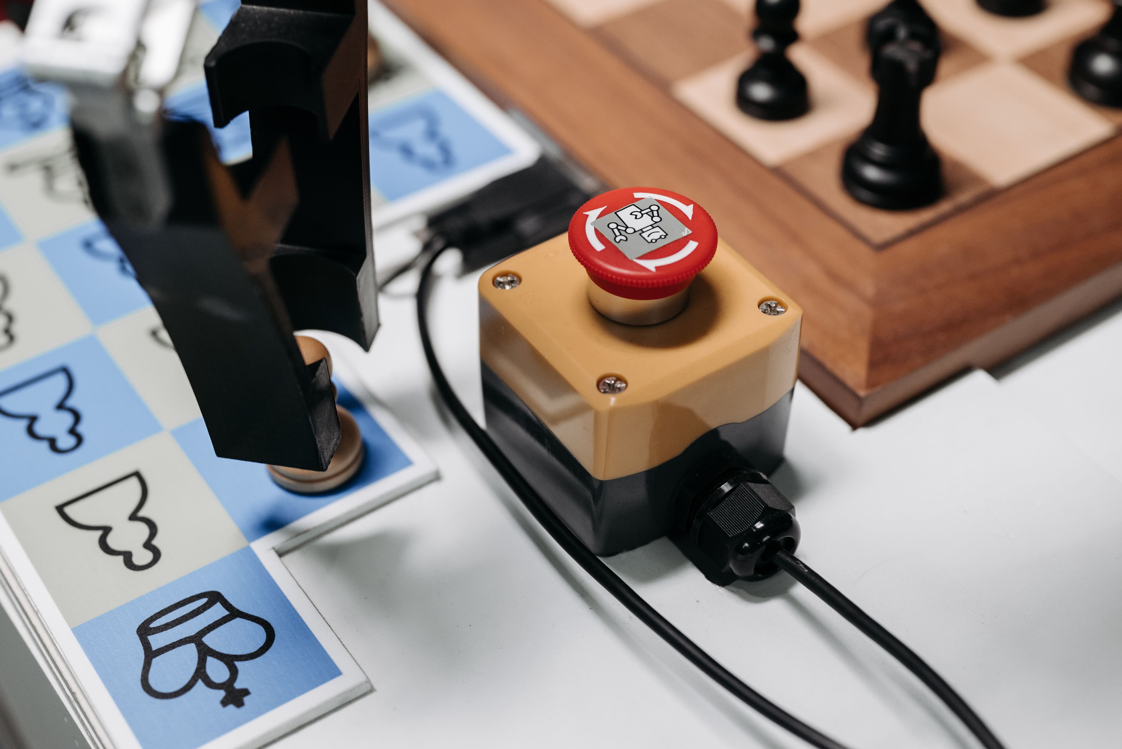 Robotic gripper beside an industrial control and chessboard.